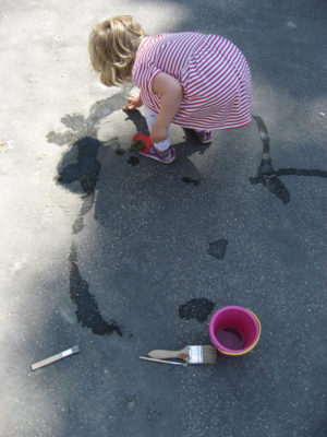 Dieťa maľuje vodou na chodníku pred domom