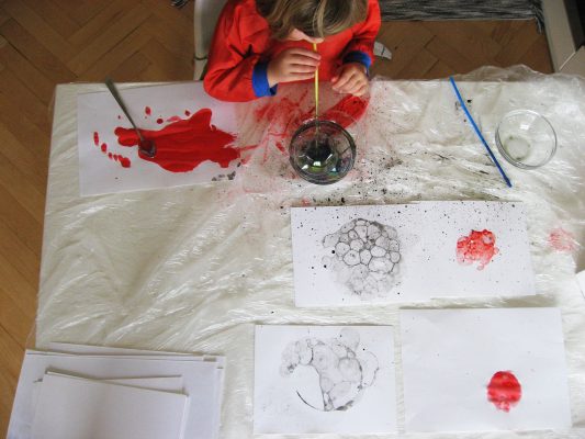 Maľovanie bublinami,dieťa fúka slamkou do farby s jarou